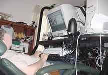 Client using a computer from a reclined position. The keyboard and monitor are on a special type of desk to allow her to have these items in the proper position when reclined.