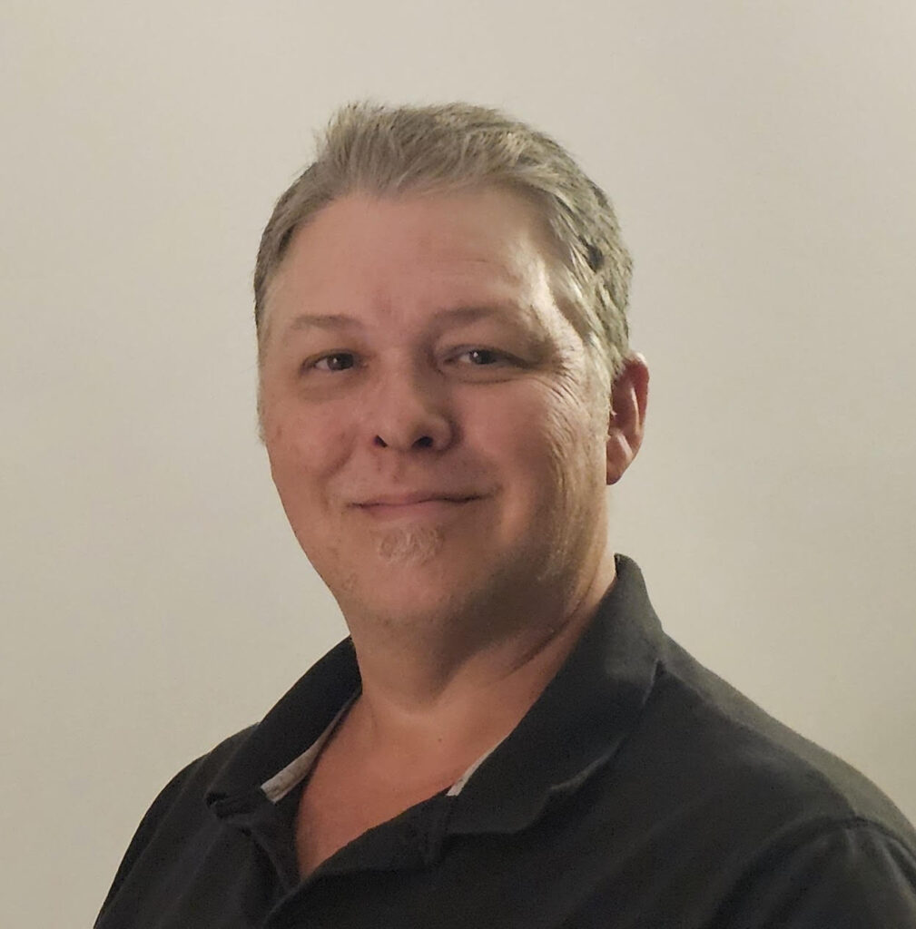 Picture of a caucasian man with blonde hair and a black polo shirt